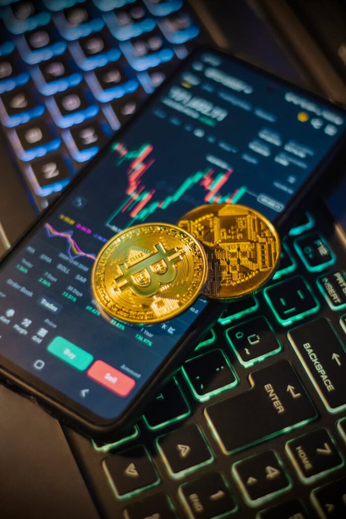 Cryptocurrency trading interface on a mobile with Bitcoin coins on a laptop keyboard.